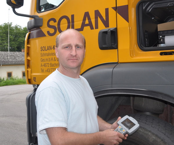 Bild von einem Fahrer der Firma Solan vor gelbem LKW mit Handheld in der Hand
